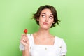 Photo of pretty doubtful lady wear white blouse eating strawberry looking empty space isolated green color background Royalty Free Stock Photo