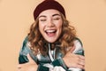 Photo of pretty excited woman in knit hat hugging herself and laughing