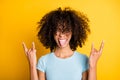 Photo of pretty funny dark skin curly woman dressed blue t-shirt showing hard rock sign tongue isolated yellow color Royalty Free Stock Photo