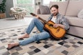 Photo of pretty handsome young man wear plaid shirt smiling sitting floor playing guitar indoors house room Royalty Free Stock Photo