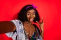 Photo of pretty impressed curly dark skin woman dressed pinup clothes tacking selfie showing hard rock sign isolated red Royalty Free Stock Photo