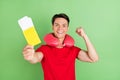 Photo of pretty lucky young man wear red t-shirt neck pillow holding tickets rising fist isolated green color background