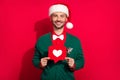 Photo of pretty sweet guy dressed xmas green cardigan holding heart like card enjoying noel isolated red color Royalty Free Stock Photo