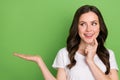 Photo of pretty tricky woman dressed white t-shirt finger chin holding arm looking empty space isolated green color