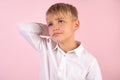 Photo of puzzled boy with stubble, scratches head, looks in bewilderment, dressed in casual white shirt, models against pink