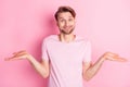 Photo of puzzled pretty young guy wear casual clothes arms hands sides not know answer pink color background