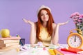 Photo of puzzled student girl throwing up hands sitting at desk with books