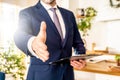 Photo of real estate or insurance agent with documents file. Man shakes the hand to the camera