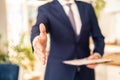 Photo of real estate or insurance agent with documents file. Man shakes the hand to the camera