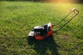 Photo of a red and black lawn mower standing on a freshly trimmed lawn during sunset. Royalty Free Stock Photo