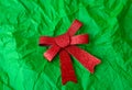 A photo of a red glittery bow on a green crumpled paper background. The bow is in the center of the image and the Royalty Free Stock Photo
