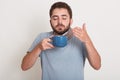 Photo of relaxing young man holding blue mug, smelling and drinking tea or coffee. Handsome guy enjoying drinking tea or coffee Royalty Free Stock Photo