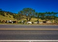 Photo of road in mountains of Minas Gerais, Brazil, with fence and pasture with livestock beside in afternoon sun and blue sky