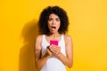 Photo of scared amazed brunette afro american woman hold phone wear white tank-top isolated on yellow color background Royalty Free Stock Photo