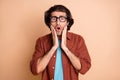 Photo of scared young man hands cheeks open mouth wear eyeglasses brown t-shirt beige color background