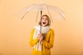 Screaming shocked woman wearing scarf holding umbrella posing isolated over yellow wall background