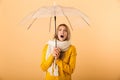 Screaming shocked woman wearing scarf holding umbrella posing over yellow wall background