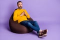 Photo of self-assured man sit beanbag hold fingers wear yellow pullover jeans shoes  purple background Royalty Free Stock Photo