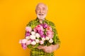 Photo of senior man hold bunch flowers smile wear checkered green shirt isolated yellow color background