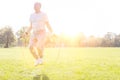 Determined senior man working out with jumping rope in park and yellow lens flare in background Royalty Free Stock Photo