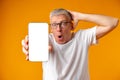 Photo of senior surprised man point finger at smartphone over yellow background Royalty Free Stock Photo