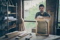 Photo of serious confident joiner in gloves uniform leaning on handmade frame looking at you pensively with planks and