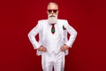 Photo of serious imposing cool old man hold hands waist wear three piece suit isolated on red color background