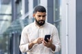 Photo of a serious Indian young man walking down the street near office buildings and using a mobile phone Royalty Free Stock Photo