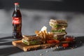 Photo session new menu of coffee house, fresh club sandwich, glass bottle Coca Cola, french fries and ketchup on wooden desk black