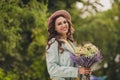 Photo of shiny adorable young woman dressed teal jacket glasses cap getting bunch wildflowers outdoors city park Royalty Free Stock Photo