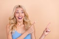 Photo of shiny impressed woman dressed blue tank-top pointing fingers looking empty space smiling beige color