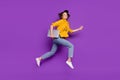 Photo of shiny pretty young woman dressed yellow shirt smiling jumping running holding modern device isolated purple Royalty Free Stock Photo