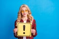 Photo of shiny sweet young lady wear plaid shirt holding exclamation point board looking empty space isolated blue color