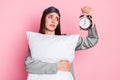 Photo of shiny unhappy young lady sleepwear holding pillow looking retro timer isolated pastel pink color background