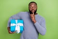 Photo of shocked afro guy wear grey pullover holding present finger lips keep secret green color background