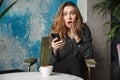 Shocked emotional beautiful young pretty woman sitting in cafe indoors using mobile phone chatting Royalty Free Stock Photo