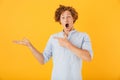 Photo of shocked european man 20s shouting and holding copyspace at palm, isolated over yellow background