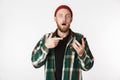 Photo of shocked man wearing hat and plaid shirt holding mobile phone, while standing over white background