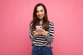 Photo of a shocked positive emotional surprised young woman posing isolated over pink wall background using mobile phone