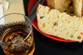 Closeup of a slice of panettone next to a knife, a glass with whiskey and ice and a gift box