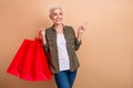 Photo of short grey hair woman khaki shirt holding red packages direct finger empty space shopping bags isolated on