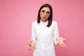 Photo shot of beautiful sorrowful young brunette woman wearing white shirt and stylish optical glasses isolated over