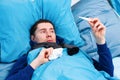 Photo of sick man in scarf with thermometer in hand lying in bed