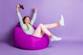 Photo of small excited lady sit beanbag hold gamepad wear green sweater pants shoes violet background