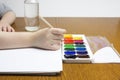 A photo of small preschooler child drawing with watercolor and brush in in the white album. Child hands and a glass of water.