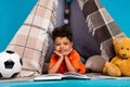 Photo of smart cute boy lying in homemade tepee reading interesting faitytale story isolated blue color background Royalty Free Stock Photo