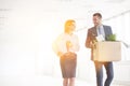 Smiling business carrying cardboard box while talking with colleague at new office and yellow lens flare in background