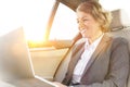 Smiling businesswoman using laptop in car with yellow lens flare in background Royalty Free Stock Photo