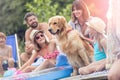 Smiling girls stroking Golden retriever while sitting with family on pier
