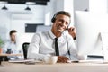 Photo of smiling operator man 30s wearing office clothes and headset, sitting by computer in call center Royalty Free Stock Photo
